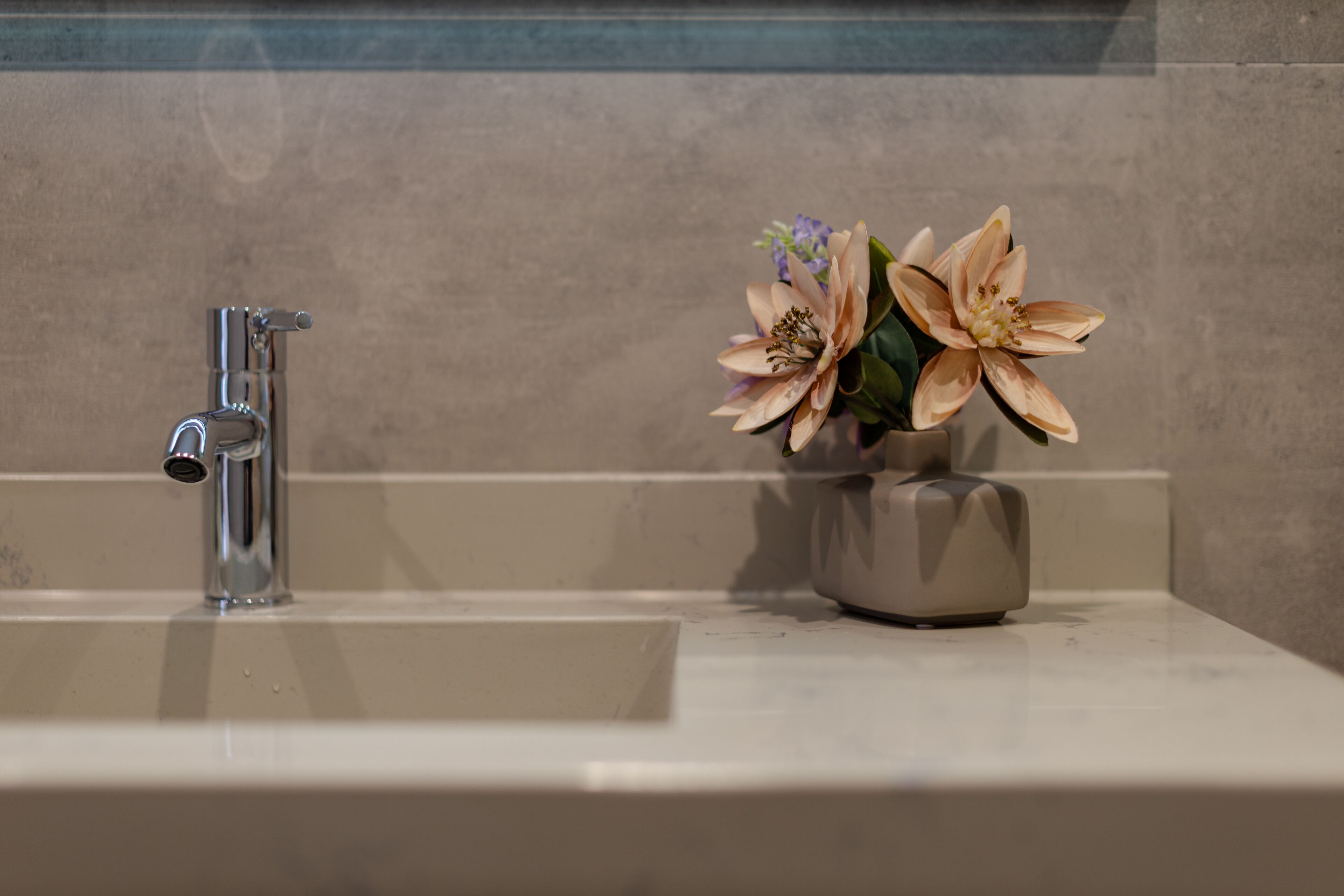 Une salle de bain avec un lavabo moderne, un robinet chromé et un vase rempli de fleurs.