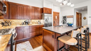 A modern kitchen with wooden cabinets, granite countertops, stainless steel appliances, and a central island with bar stools. - Luxury Resort Penthouse at Peak 9 Base/on Main St. (Breckenridge)