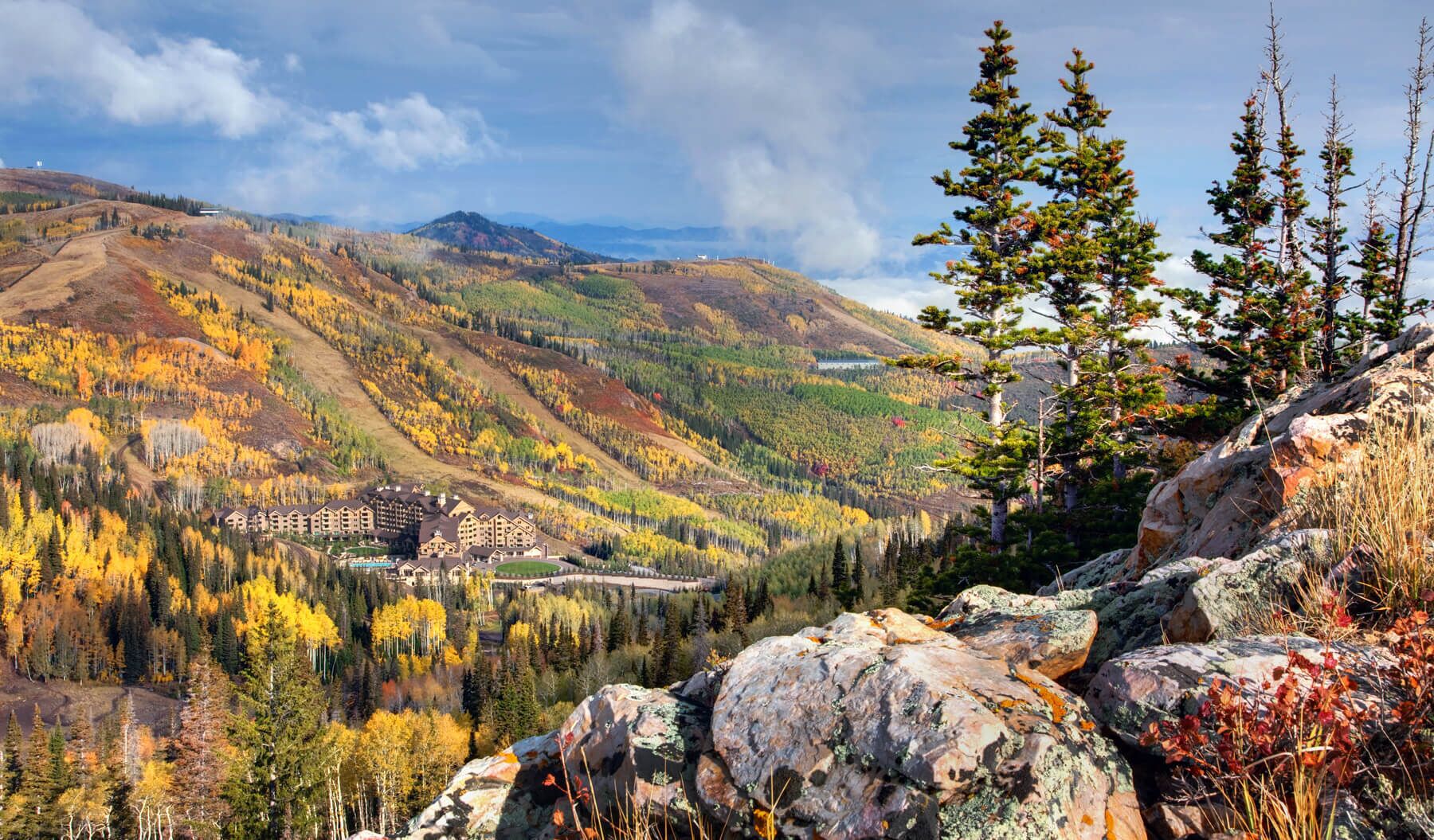 A mountain lodge with multiple buildings, surrounded by autumn-colored trees and rocky terrain.