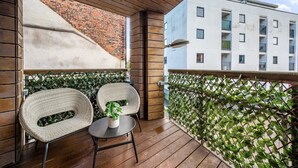 A balcony with two wicker chairs, a small table, and a potted plant. A brick wall and a white building with balconies are visible in the background. - Host & Stay | Ropewalks Quarters V (Liverpool)