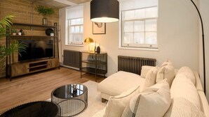 Ein modernes Wohnzimmer mit Sofa, Fernseher, Couchtisch und Lampe.