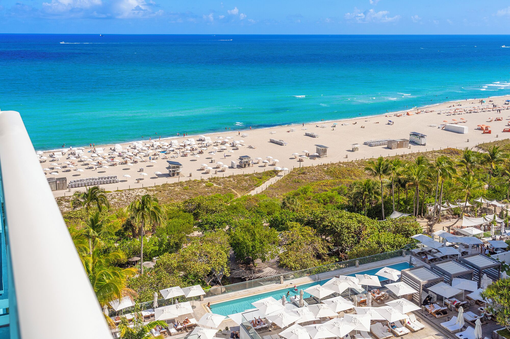 Un resort frente a la playa con piscina, sombrillas y vistas al océano.