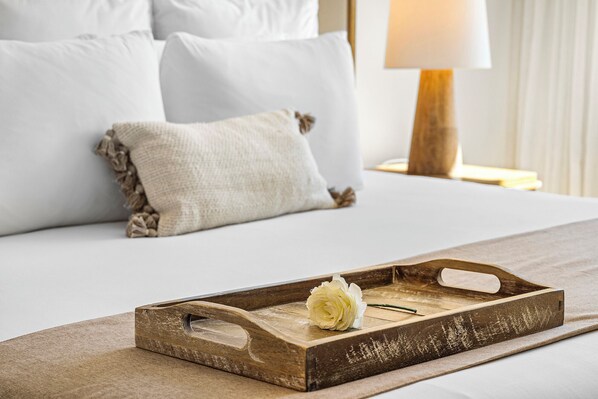 A wooden tray with a white rose on a bed with white bedding and pillows.