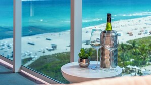 A table with a bottle and glasses, a small plant, and a view of a beach and ocean.