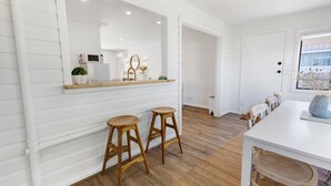 Una cucina con pareti in legno bianco, un grande specchio, due sgabelli di legno e un tavolo da pranzo bianco.