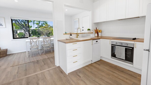 Una cucina moderna con mobili bianchi, un piano di lavoro in legno e un forno integrato.