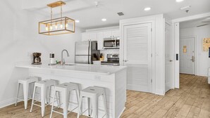 A modern kitchen with a large island, bar stools, stainless steel appliances, and a pendant light.