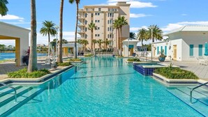 A swimming pool surrounded by palm trees and a multi-story building with balconies.
