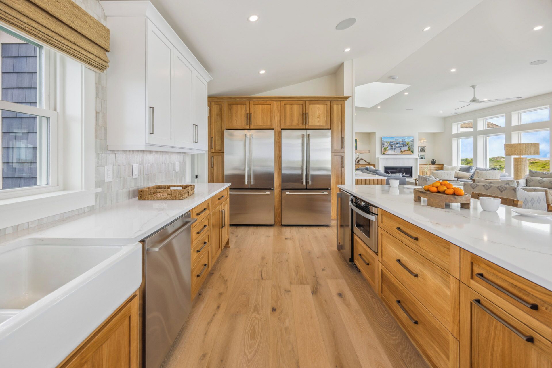 A modern kitchen with wooden cabinets, stainless steel appliances, and a large island with a bowl of fruit.