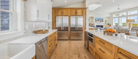 A modern kitchen with wooden cabinets, stainless steel appliances, and a large island with a bowl of fruit.