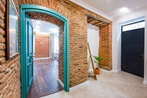 Un corridoio con pareti in mattoni, una cornice della porta color verde acqua, una pianta in vaso e una porta nera.