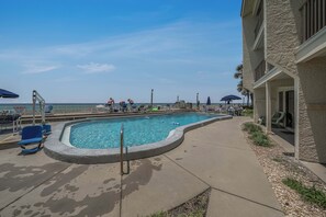 A swimming pool with a concrete edge, a concrete deck, and a view of the ocean.