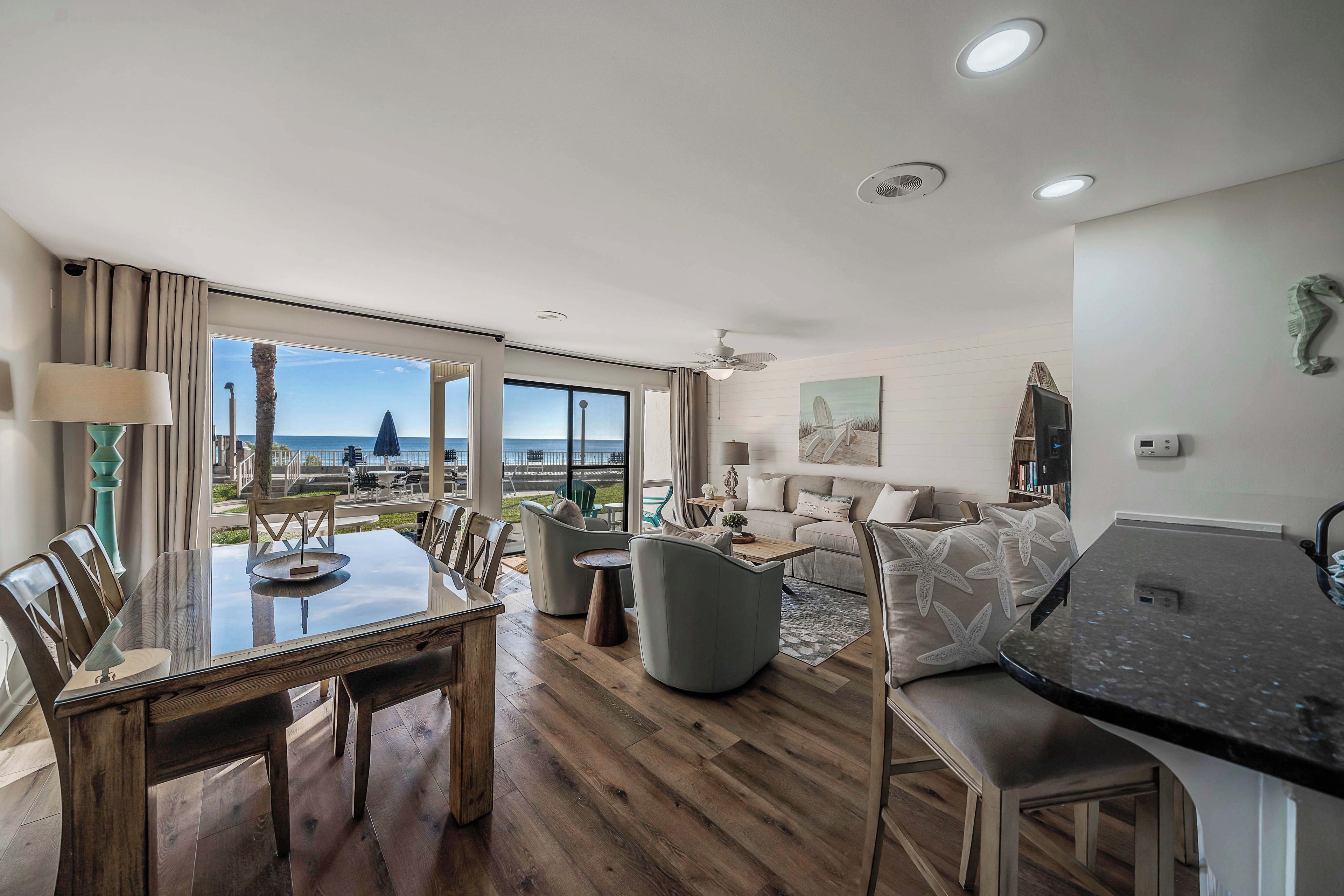 A spacious living area with a large window offering a view of the sea, a dining table with chairs, a sofa, and a coffee table.