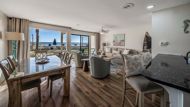 Amplia sala de estar con un ventanal que ofrece vistas al mar, una mesa de comedor con sillas, un sofá y una mesa auxiliar.