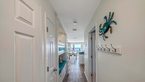 Un pasillo estrecho con puertas blancas, una cama nido, un comedor con mesa y sillas, y una decoración de cangrejo colgada en la pared.