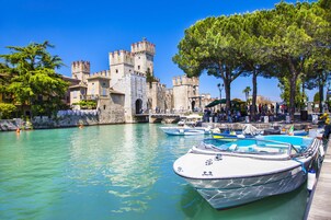 A historic castle with a moat, boats docked in the water, and a crowd of people.