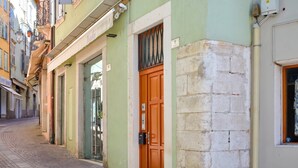 Une rue étroite bordée d’immeubles, avec une porte verte et un mur de briques.