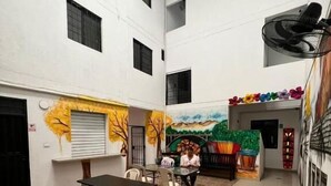 Un espacio interior amplio con techo alto, una mesa central con sillas y un mural en la pared que representa un paisaje.