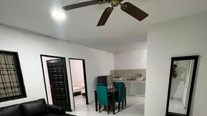 Una sala moderna con un sofá seccional negro, una mesa de comedor con sillas color turquesa y una cocina al fondo.