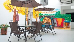 Un comedor con mesas y sillas, un mural con árboles y un puente, y una planta en maceta.