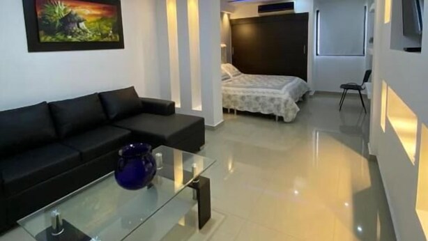 Una sala moderna con un sofá negro, una mesa de centro de vidrio y un cuadro en la pared.