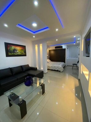 A modern living room with a black sofa, a glass coffee table, and a painting on the wall. - Aparta Hotel El Cacique Upar (Valledupar)