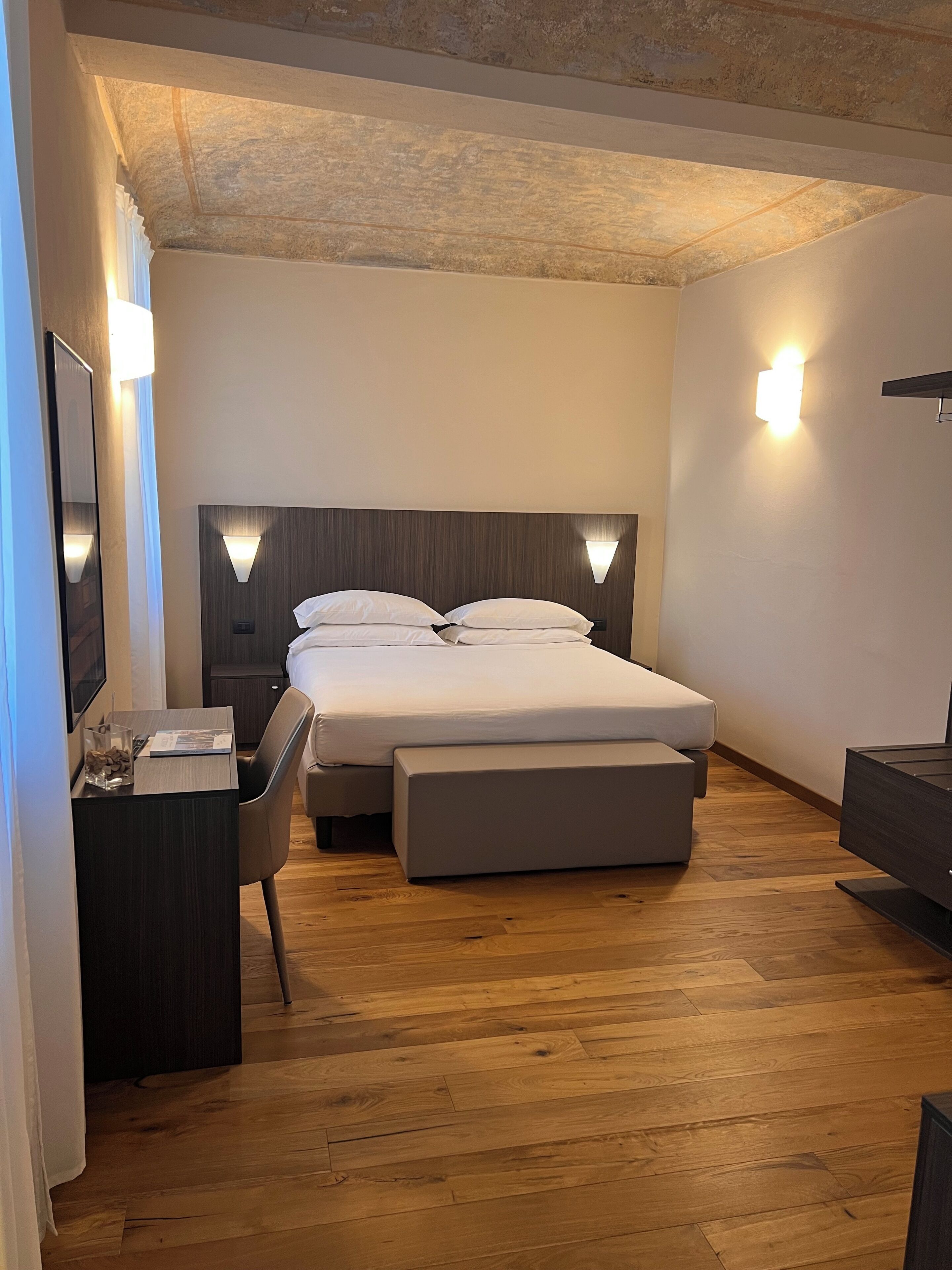 A modern bedroom with a wooden floor, a bed with a headboard, bedside tables, and a desk with a chair.
