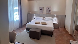Habitación de hotel moderna con una cama grande, lámparas de noche, una mesita y vistas al exterior por la ventana.