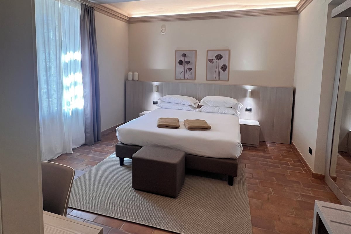 A modern hotel room with a large bed, bedside lamps, a small table, and a view of the outside through the window.