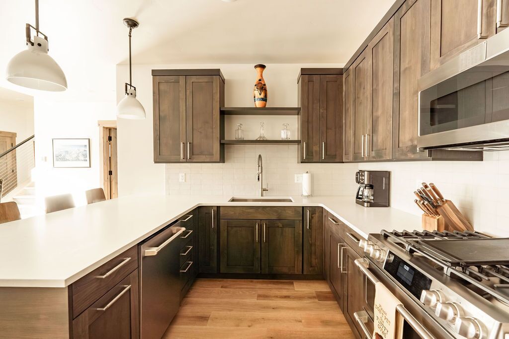 A modern kitchen with dark wooden cabinets, a white countertop, stainless steel appliances, and pendant lighting.