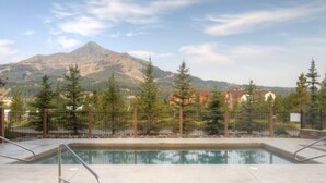 A rectangular pool with metal railings, surrounded by a fence and trees, with a mountain in the background. - Luxury 4BR Big Sky Condo | Steps to Resort, Hot Tub & America's Best Skiing (Big Sky)