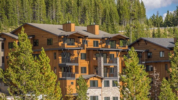 A multi-story lodge with wooden exteriors and balconies, surrounded by pine trees. - Luxury 4BR Big Sky Condo | Steps to Resort, Hot Tub & America's Best Skiing (Big Sky)