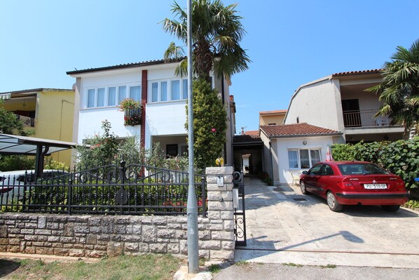 A residential area with a white house, a red car parked in front, and a stone wall.