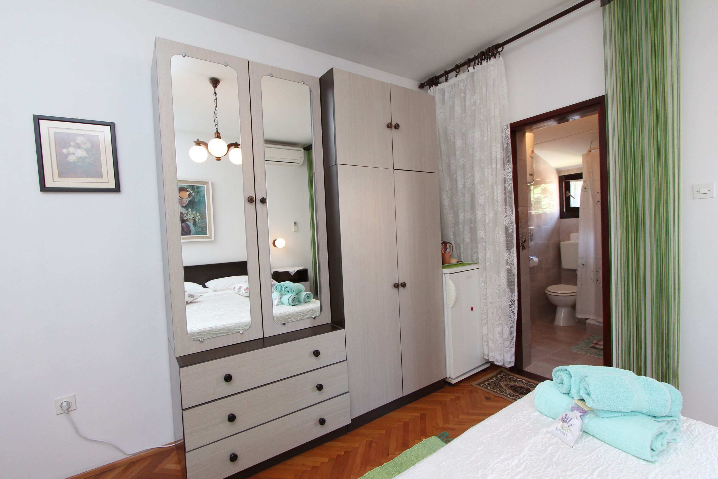 A bedroom with a bed, a wardrobe, a mirror, and a bathroom visible through an open door.