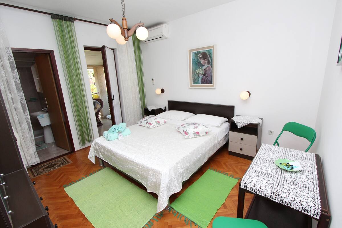 Ett sovrum med en säng, sängbord, en stol, ett bord och en tavla på väggen.
