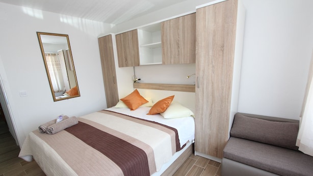 Ein ordentlich eingerichtetes Schlafzimmer mit Bett, einer Couch, einem Spiegel und eingebauten Holzschränken.