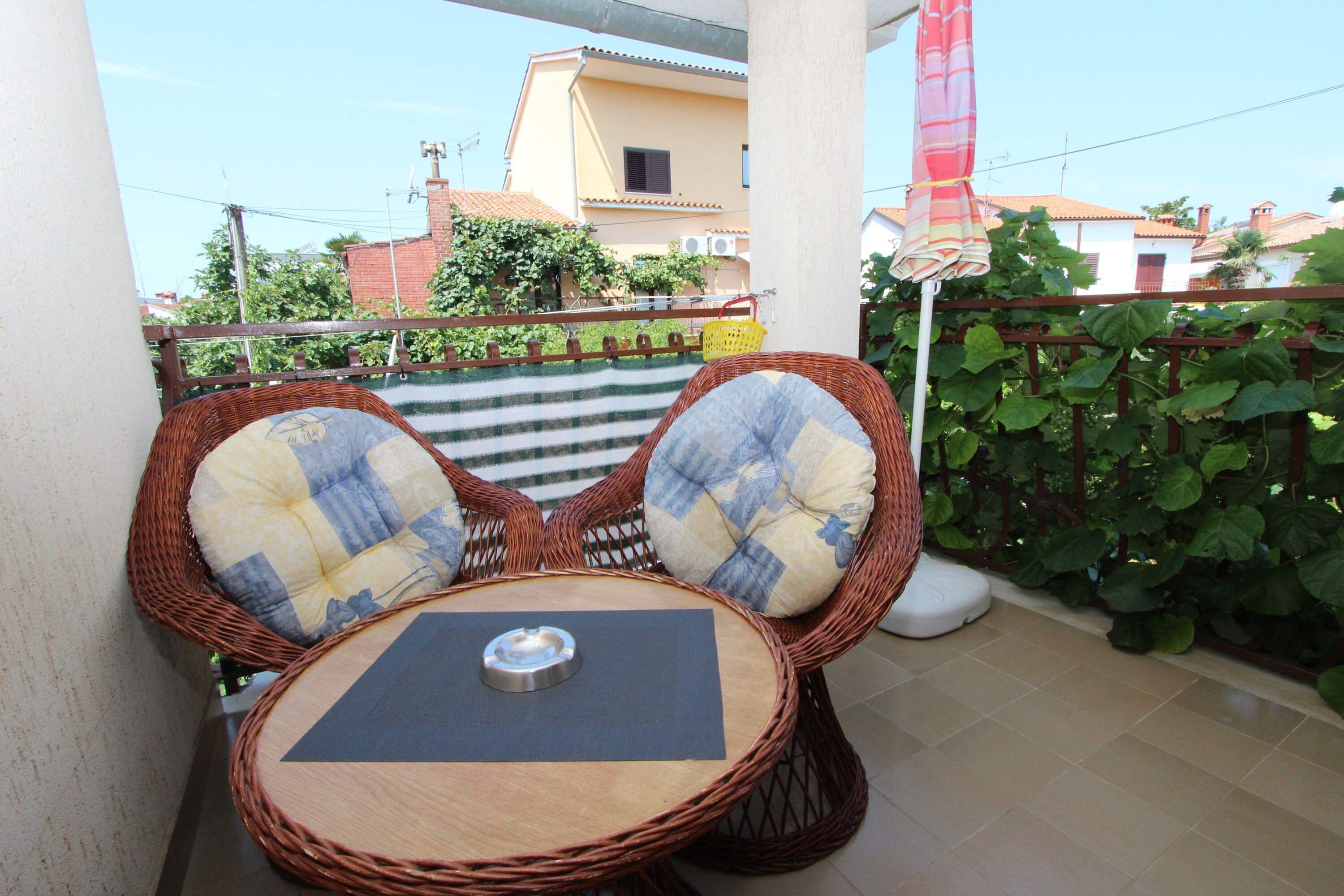 A wicker table with two chairs and a metal ashtray on a balcony.