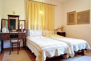 A bedroom with two single beds, a desk with a chair, a mirror, and two lamps.