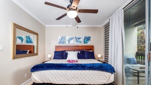 Ein Schlafzimmer mit Bett, Deckenventilator, Kunstwerken und Blick durch eine Schiebetür.