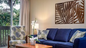Ein Wohnzimmer mit einem blauen Sofa, einem Holztisch und einem Sessel mit tropischem Blattmuster.