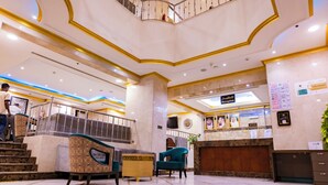 A hotel lobby with marble flooring, a reception desk, a staircase, and a seating area with patterned chairs. - Diyafa Al Mukhtara Hotel (Madinah)