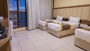 A hotel room with two beds, a large window with curtains, a bedside table with a phone, and a view of buildings outside. - Diyafa Al Mukhtara Hotel (Madinah)