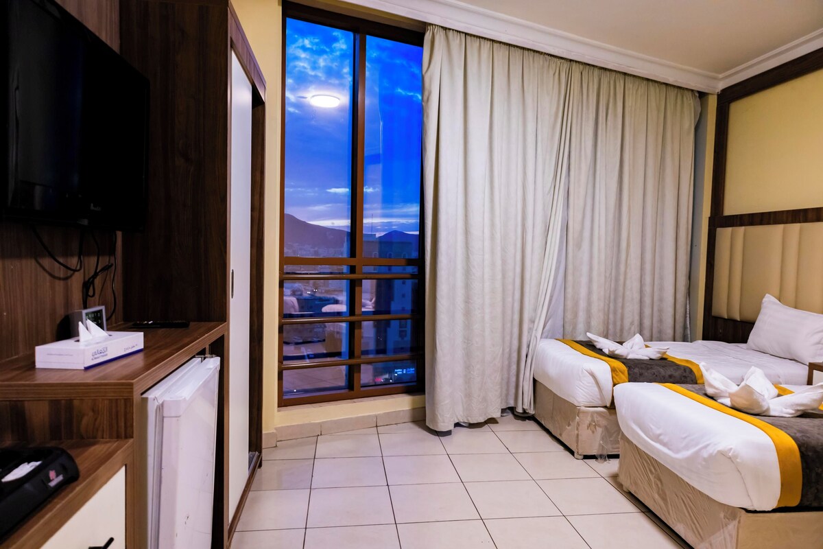 Une chambre d’hôtel avec une grande fenêtre, un lit, une télévision et un bureau équipé d’un ordinateur et d’une boîte de mouchoirs.