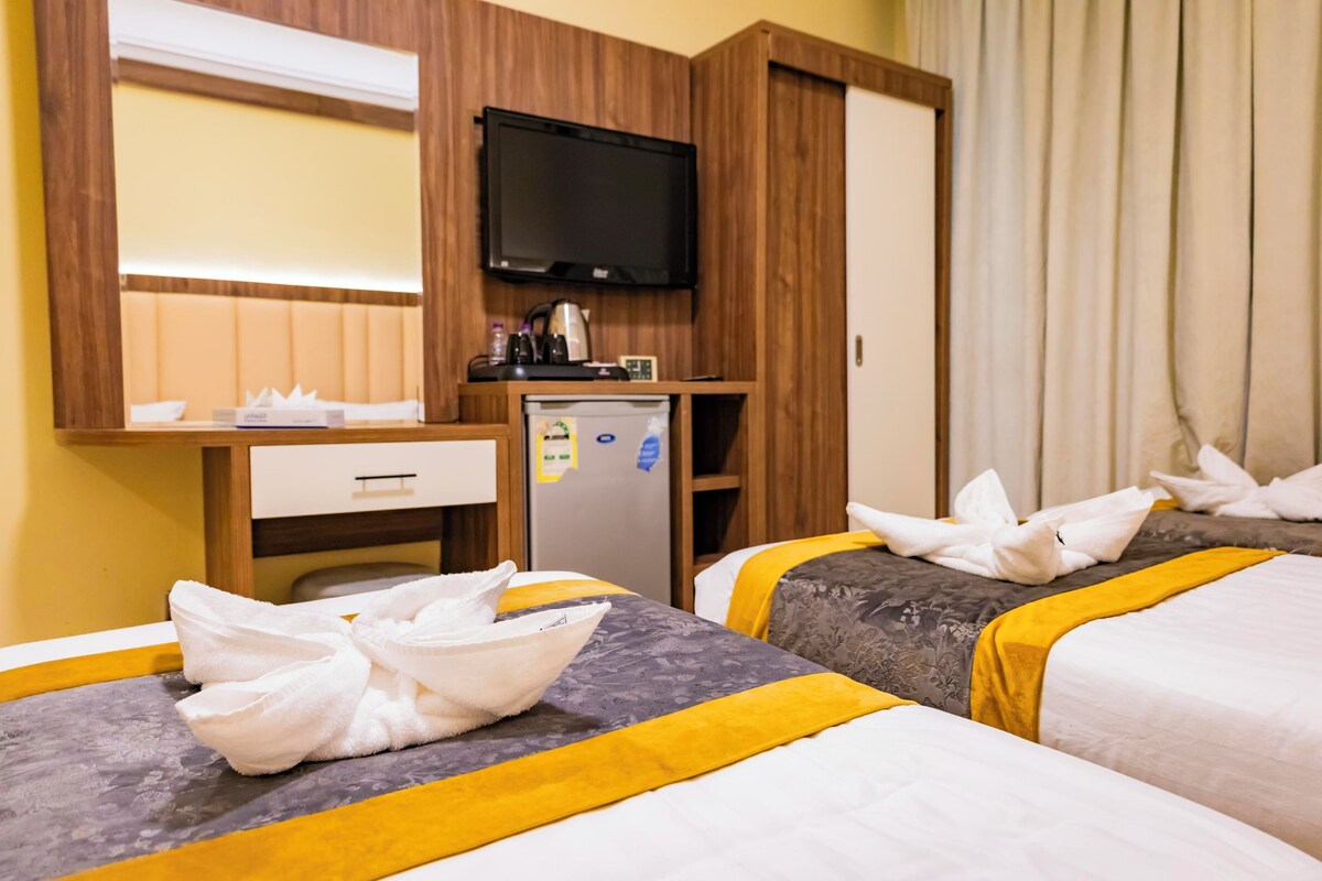 A hotel room with two beds, a television, a minibar, and a desk with a drawer.