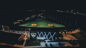 Un estadio con césped verde, un logotipo iluminado de gran tamaño y un área de estacionamiento.