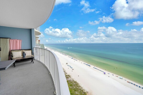 A balcony with a view of a beach, a sofa, and an owl decoration.