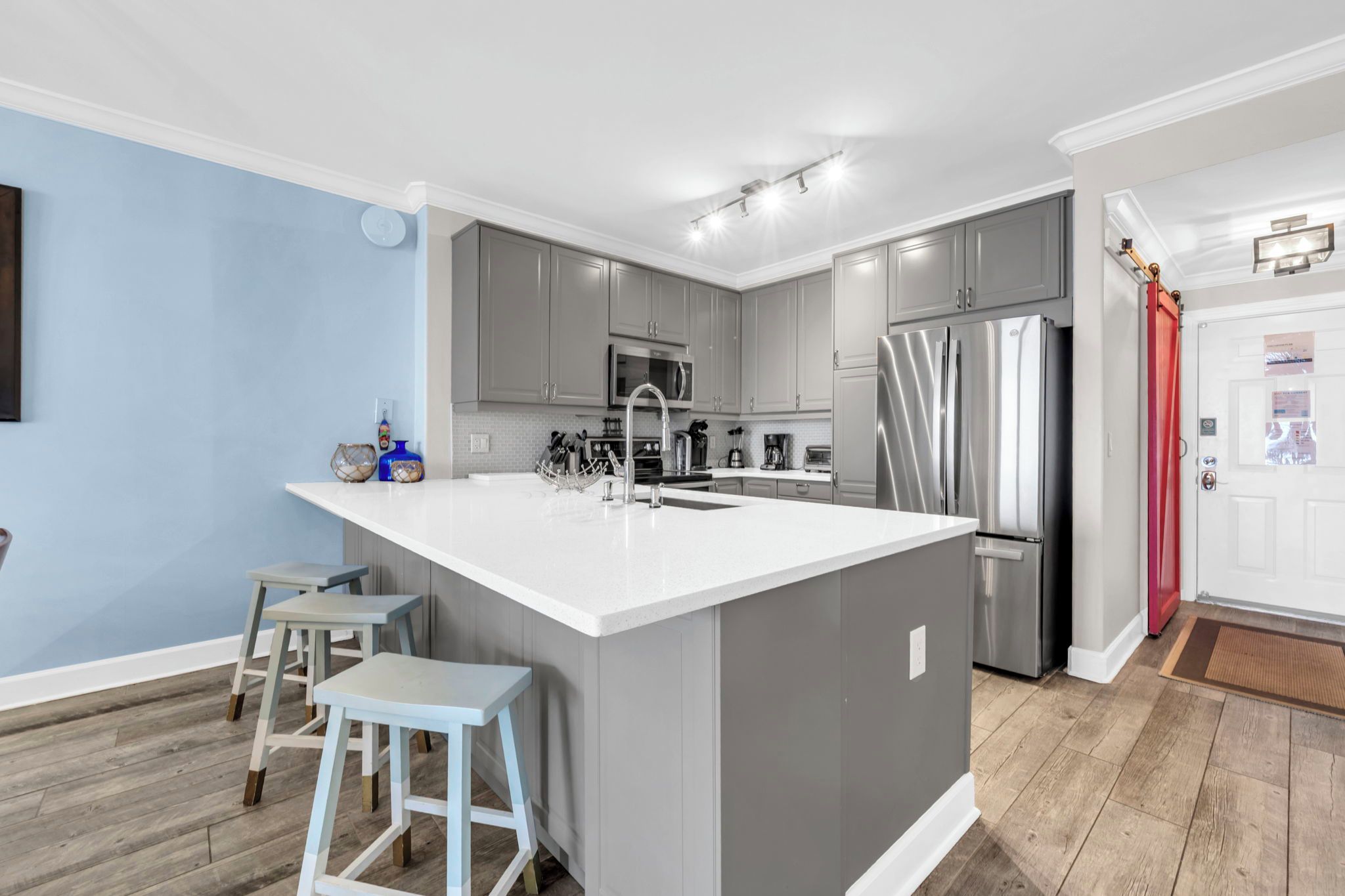 A modern kitchen with grey cabinets, a stainless steel refrigerator, and a white island with bar stools.