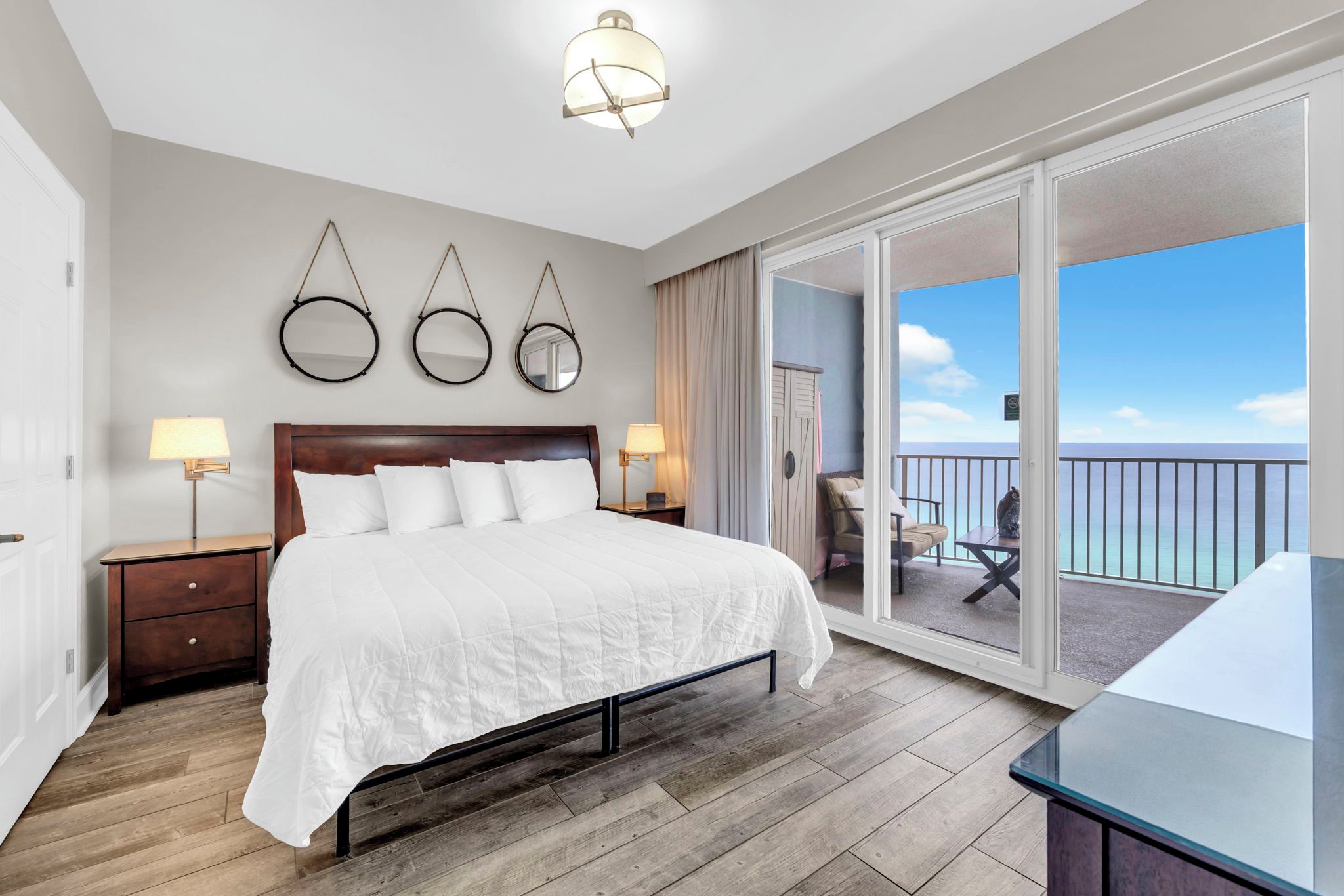 Habitación de hotel con una cama grande, lámparas de noche, piso de madera y un balcón con vistas.