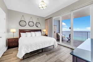 A hotel room with a large bed, bedside lamps, a wooden floor, and a balcony with a view.