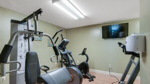 Un gimnasio en casa con una máquina de press de banca, una elíptica, una bicicleta estática y una cinta de correr.